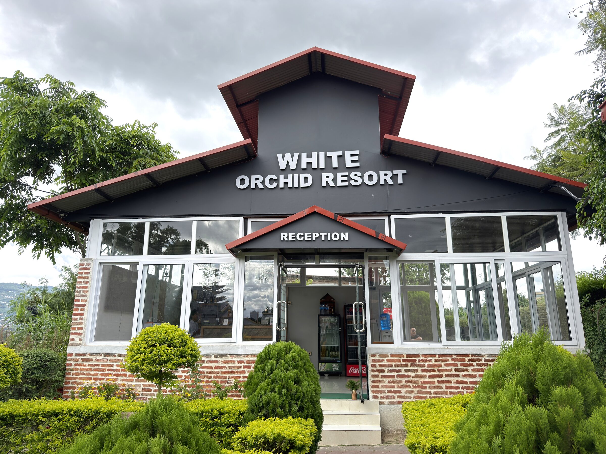 White Orchid Resort reception building with brick facade and red-roofed gable, surrounded by manicured hedges